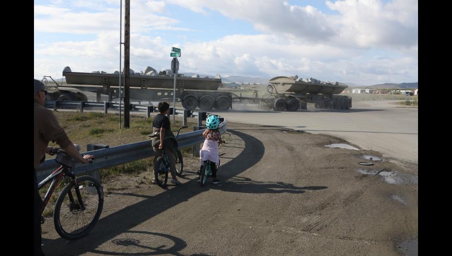 A Kiewit haul truck transports rock for the Nome Port Expansion project to the harbor as young bicyclists yield, at the intersection of the Snake River bridge and Seppala Drive, on July 21.
