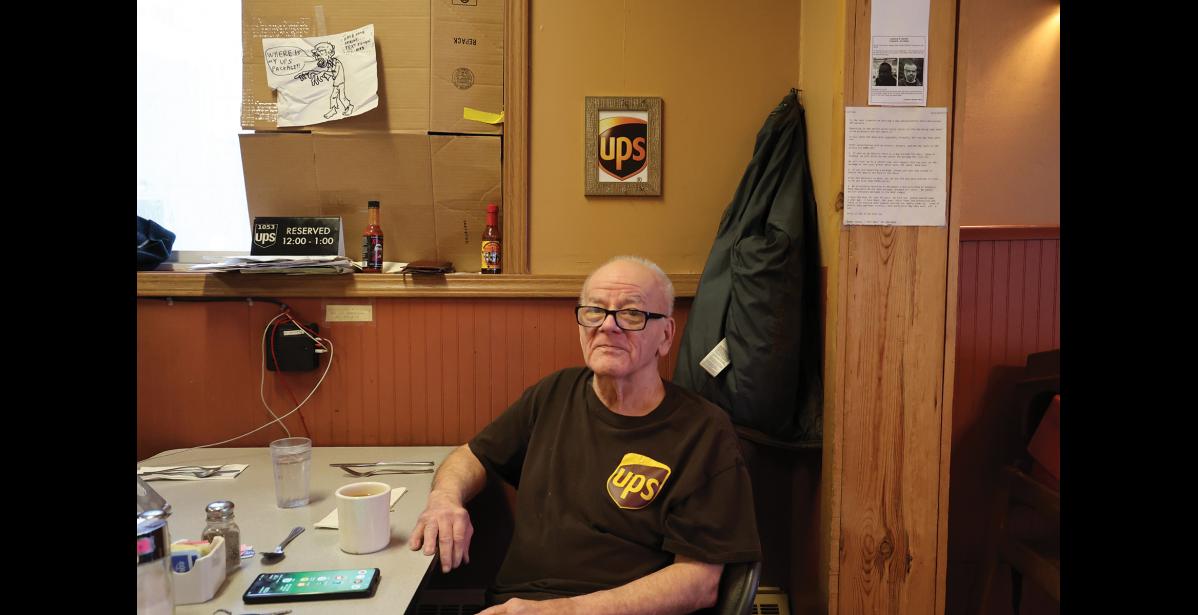 Photo by Anna Lionas MOST VALUABLE CUSTOMER–Ramon Gandia sits at his reserved table in the Polar Café. Every weekday from 12 p.m. to 1 p.m. he is open for UPS business at the cafe.