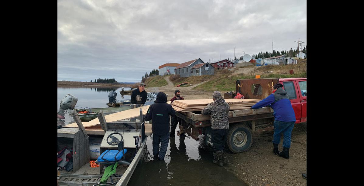 Photo by Yorise Yakunin HANDOFF—The transport crew loads planks of plywood from a riverboat into the bed of a truck in White Mountain. The materials were driven from Nome to Council on the road, and then taken by boat to White Mountain.